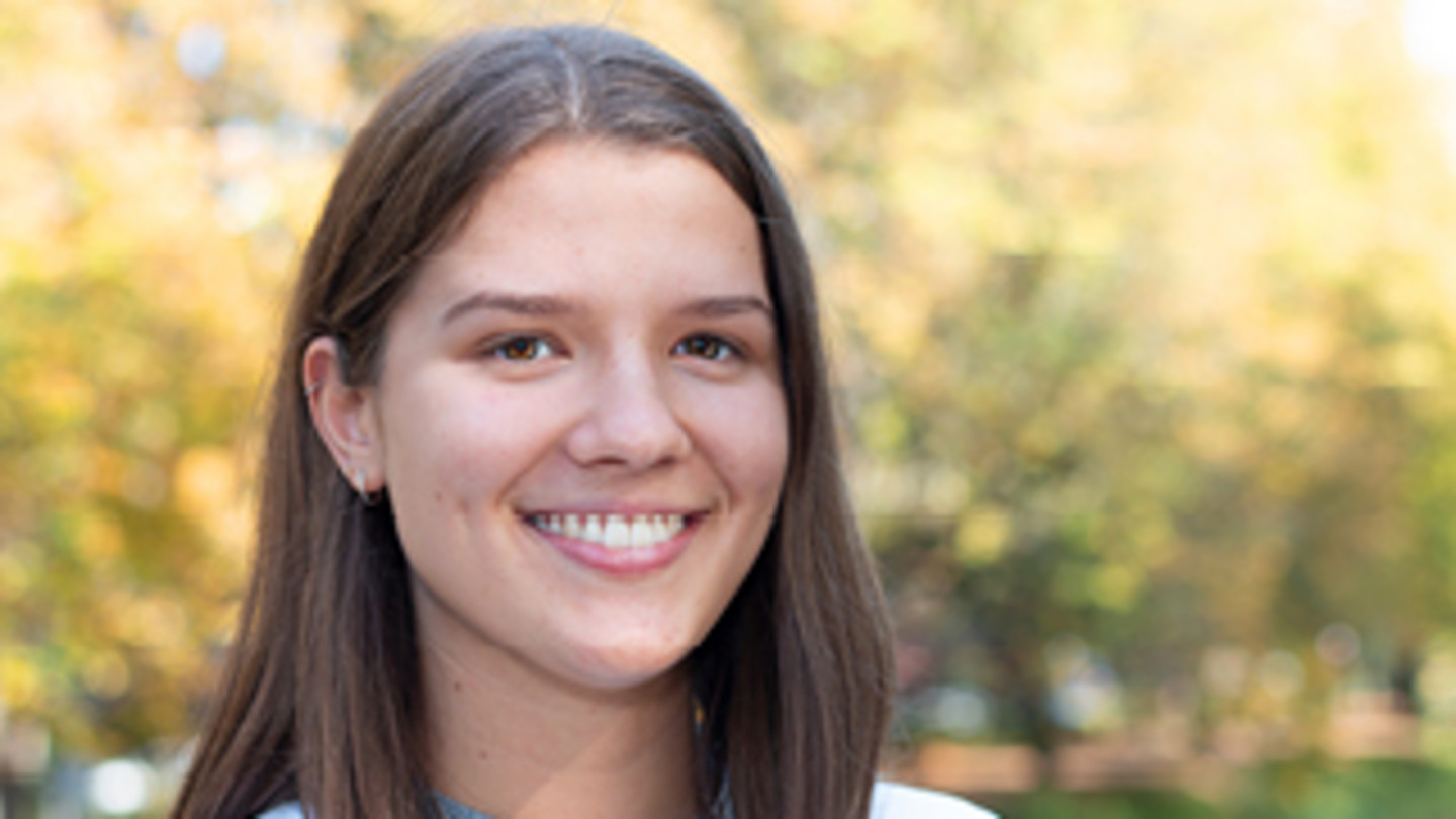 Closeup of WiSo-Student Lena in front of autumnal trees - Text: „Today’s Ideas. Tomorrow‘s Impact – My idea is to become the best version of myself by identifying my strengths and use them to have a small but positive impact on our world and society“